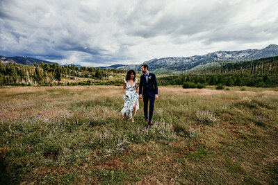 Bride and groom embracing on the sandy shoreline at Sand Harbor in Lake Tahoe, with calm blue water, large granite rocks, and snow-capped mountains in the distance at sunset.