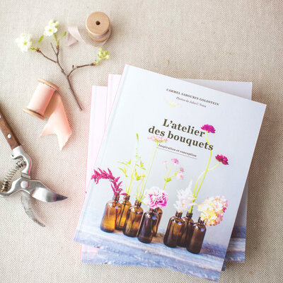 A book about flower arranging sits on a table, surrounded by tools and flower blooms. 