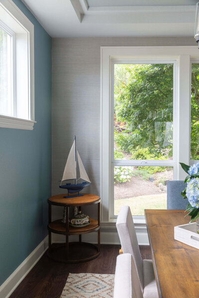 A corner of a formal dining room featuring a corner table with a small sail boat sitting on top of it showcasing a coastal interior design.