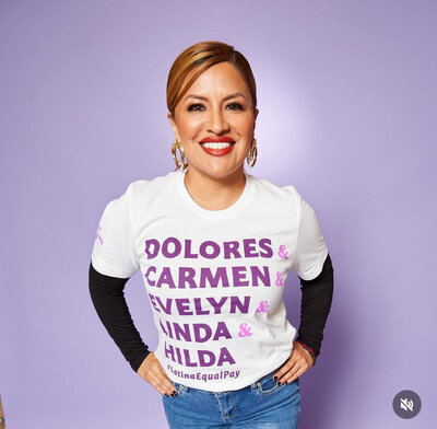 Member of LAU smiling in a white and black layered shirt with influential Latina names printed on it, posed in front of a purple background.