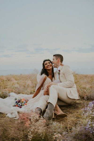 A bride and groom sitting on the ground outside