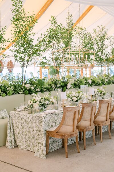 Table at a wedding reception with green and white floral tablecloth and flowers