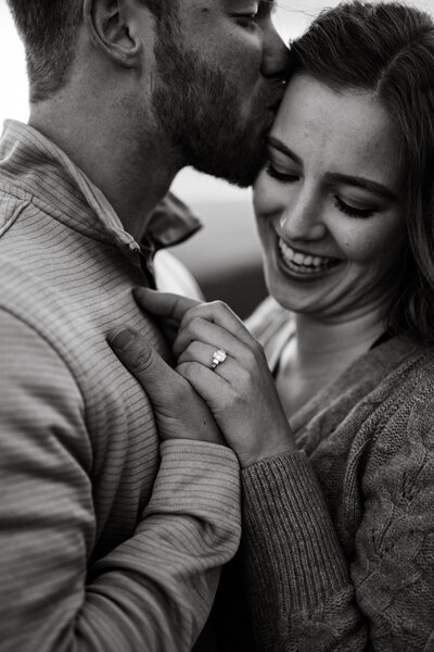 photo of an engaged couple with an engagement ring smiling