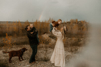 Family of four twirling and dancing in a gravel pit with their dog by their side.