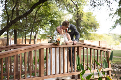 An Austin-based wedding photographer captures a tender moment as the bride and groom share a passionate kiss on a scenic wooden bridge.
