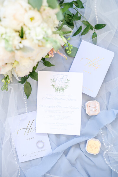 His and her vow books and invitation suite on light blue background during wedding details photographed by Wedding Photographer in Baltimore, MD