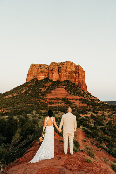 bride and groom in sedona holding hands on baby bell rock after eloping at sunset