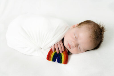 newborn boy sleeping in white wrap with small rainbow