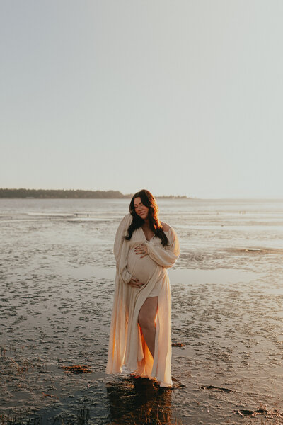 Photo of a pregnant woman holding her belly while standing on a beach taken by a langley family & newborn photographer
