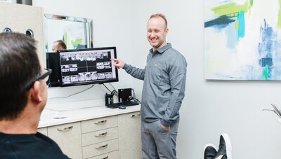 Prosthodontist Dr. Tyson Merrill explaining a dental X-ray to a patient while discussing custom veneers at Peak Prosthodontics in Lethbridge, Alberta.