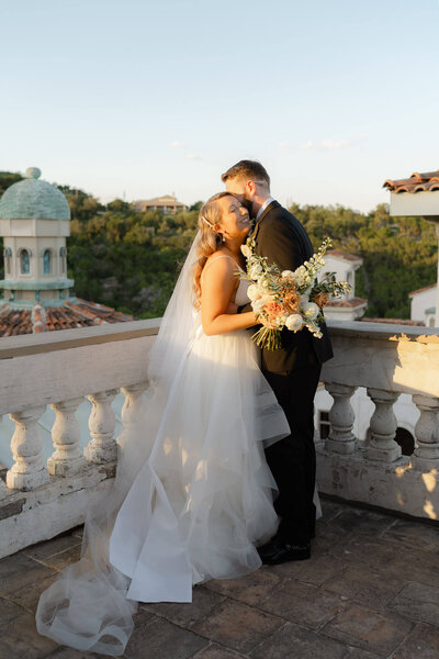 bride and groom embracing on a balcony overlooking Villa Antonia