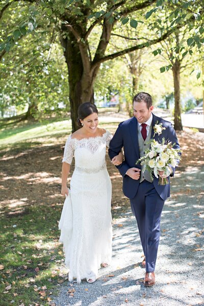 Bride and groom smile and walk through park together