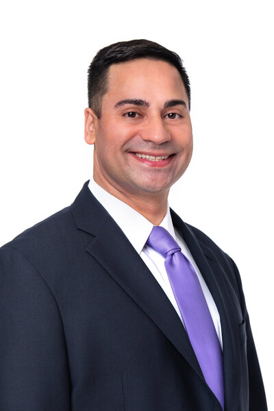 A Caucasian man with a suit and periwinkle colored tie smiling and posing in front of a white backdrop at his headshot session.