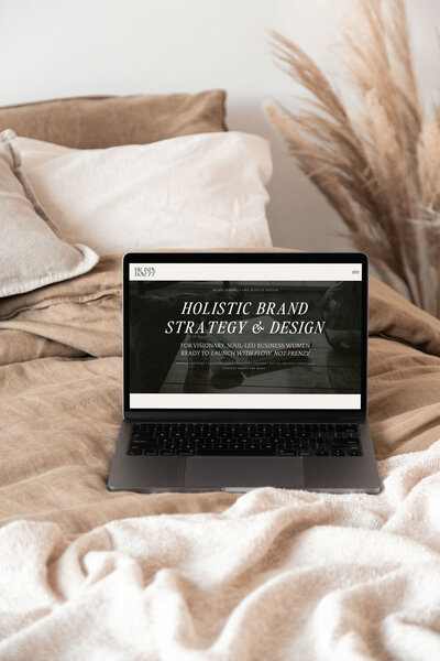 macbook with brandy boyett homepage screen sits on bedding
