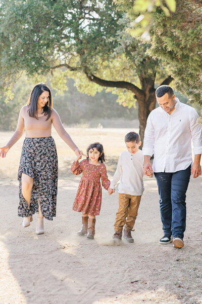 Two little boys stand on a sandy path holding hands for their family portraits in Austin, TX. They wear matching plaid shirts and blue jeans.