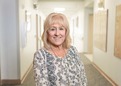 A woman smiling stands in a bright white hallway.