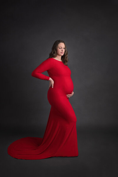 side profile of prenant woman in red dress cradling her belly with one hand