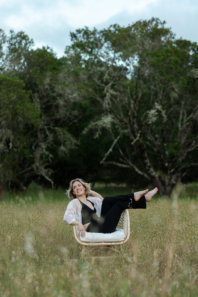 Woman sitting in a chair with her legs up on the side of the chair in an outdoor California field.