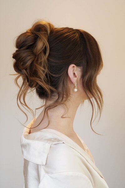 Bride wearing a high bun with statement earrings — sleek and sophisticated wedding hairstyle by Klover Beauty.