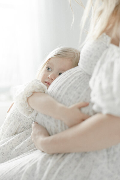 Toddler girl holding mother's belly