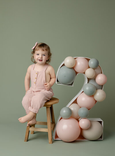Toddler girl sitting on stool with balloon filled #2 marquee. Set up was created by Jenni Nikki Photography at her Woodstock Photo Studio near Atlanta GA.