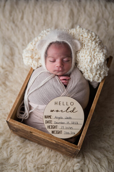 Newborn baby boy snuggled up sleeping in a crate