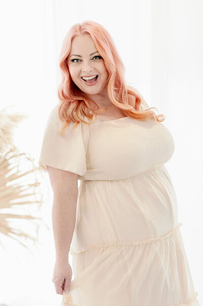 Head stylist Kandra sits on white couch in white dress with pink hair 