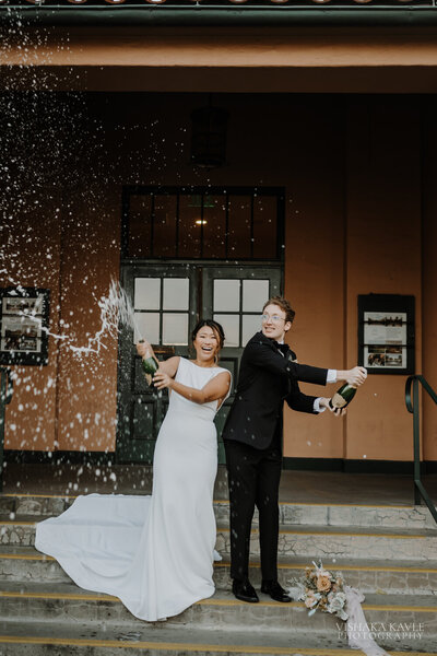 bride and groom laughing while popping champagne.