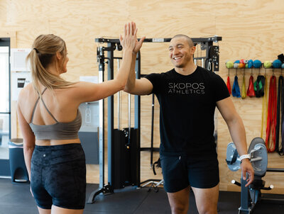 A Skopos Athletics coach and gym member high-fiving in Dundas, MN, celebrating progress and a strong fitness community.