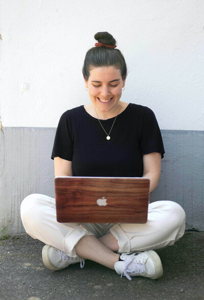 Woman with a laptop on her lap sitting cross-legged in front of a grew wall