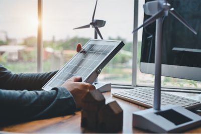 Image of hands holding a solar panel in front of a model-sized wind turbine