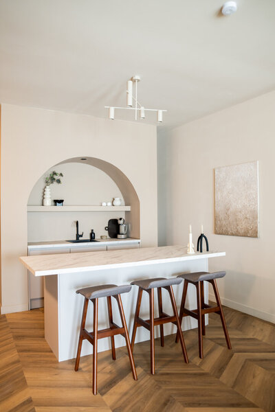 Minimalistisch ingerichte slaapkamer in Studio Laurant met een bed tegen vier bogen aan de hoofdbordzijde en een houten voetenbankje aan de voetenzijde, in een serene en stijlvolle setting.