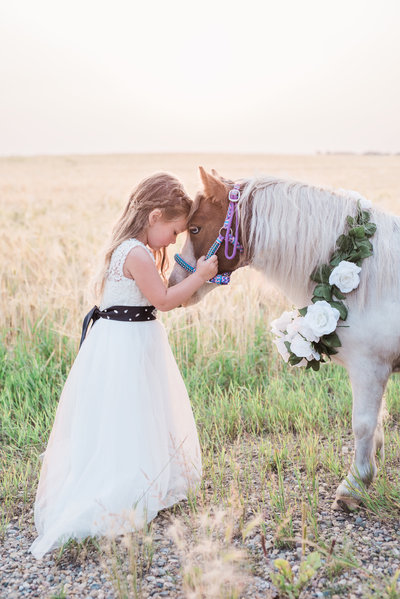 little girl touching a pony's head in a open field