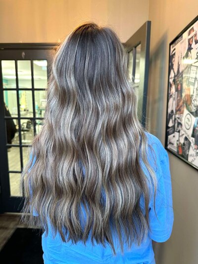 A back view of a woman with long, beachy waves, showcasing a relaxed and stylish hairstyle created by 212 Salon, Spa, & Barbershop.