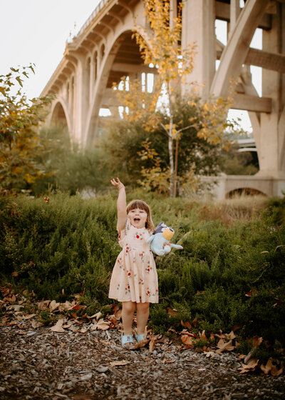 excited toddler girl in dress holding her bluey toy under the Colorado street bridge during her family photos in Pasadena, California 