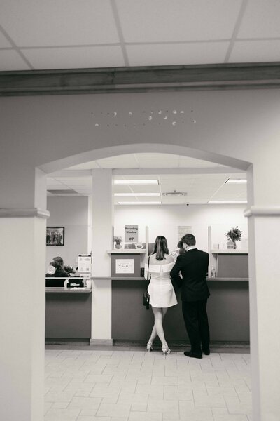 Elopement photos - Getting Married at St. Augustine Courthouse | A couple stands at the counter inside the St. Johns County Courthouse in St. Augustine, preparing for their civil ceremony. Captured in a quiet, documentary style by a St. Augustine elopement photographer, this black-and-white photo highlights the intimacy of a courthouse wedding at the St. Johns County Courthouse Wedding Chapel.