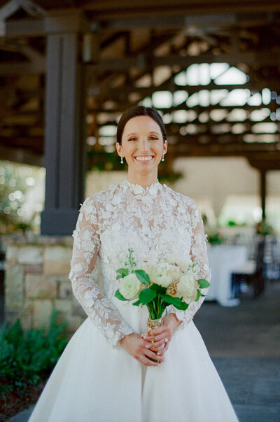 woman in lace white dress smiling holding a bouquet of white flowers