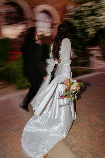 bride and groom run off into the distance with brides after party dress trails behind her