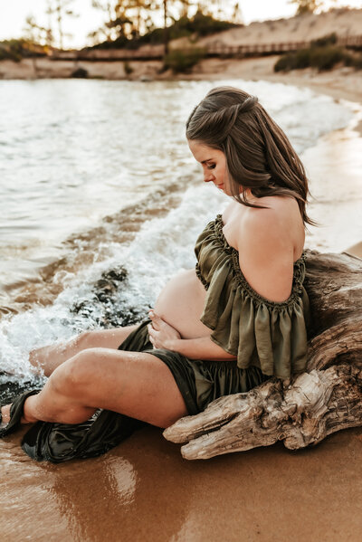 Pregnant mother sitting against driftwood on the Tahoe beach.