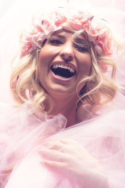A woman wearing a floral crown and wrapped in pink tulle is lauging.