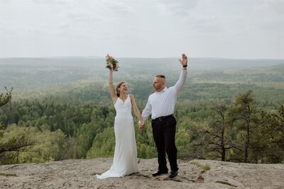 eloping couple celebrating after saying vows on a rocky overlook with pine trees in the distance 
