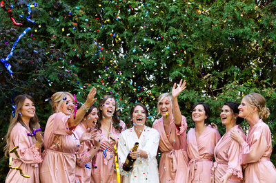 a bride and her bridesmaids in pink robes cheer as confetti explodes during the bride's Ottawa wedding photos