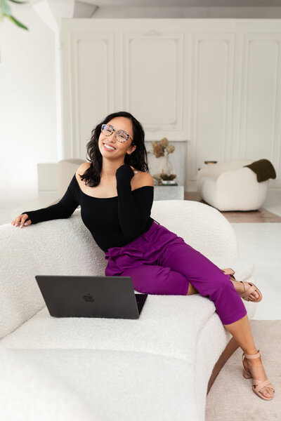 Anh Nguyen, photographer, smiling with a computer on the couch.