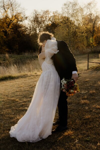 Newlyweds drenched in golden sunlight share a romantic kiss under Iowa fall foliage.