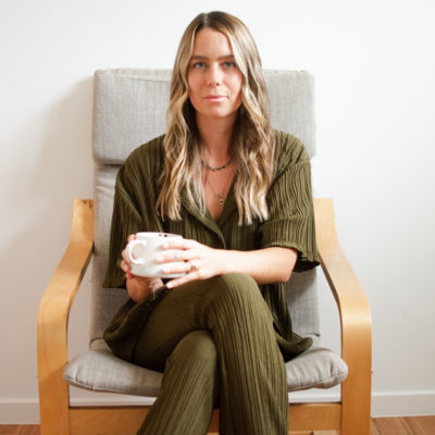 Tahlia Swartz sitting in a chair by a white wall holding coffee