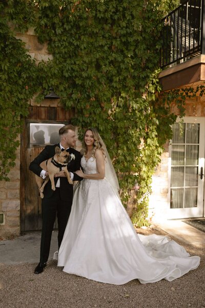 Bride and groom pose with dog, dressed in black tie, at their Italian inspired Colorado wedding. 