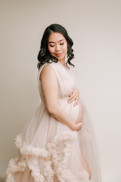 Portland mom in pink dress in  Portland Studio. her daughter is kissing her belly.