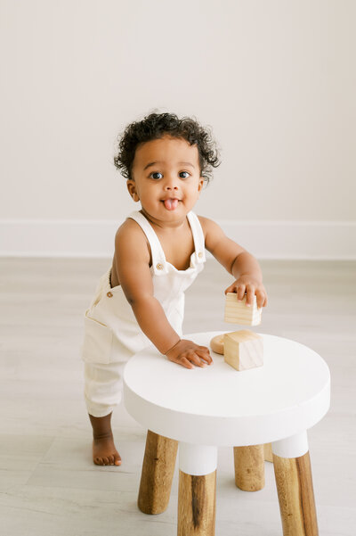 Baby boy with dark curly hair plays with wooden blocks during studio photography session.