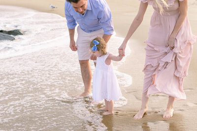 little girl walking in waves holding parents hands