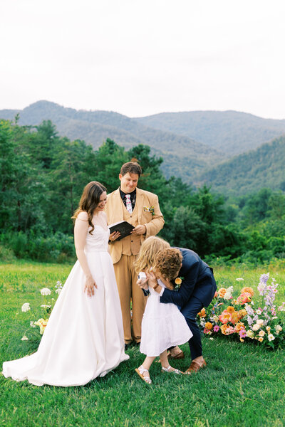 The groom embraces the ring bearer during the ceremony at Paint Rock Farm in North Carolina, a scenic wedding venue, by photographer My Sun and Stars Co.